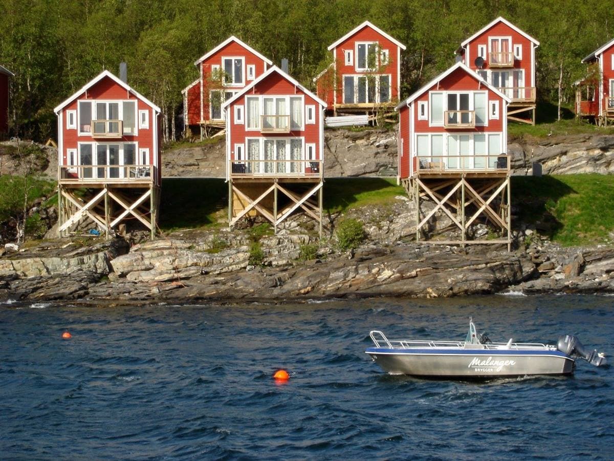 Red waterfront cabins on stilts seen from the fjord, with a boat in front