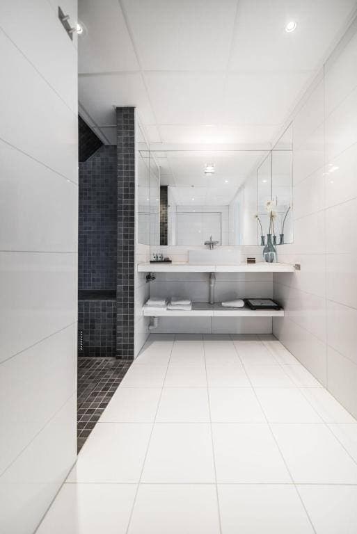 Bright hotel bathroom with white tiles and a walk-in shower