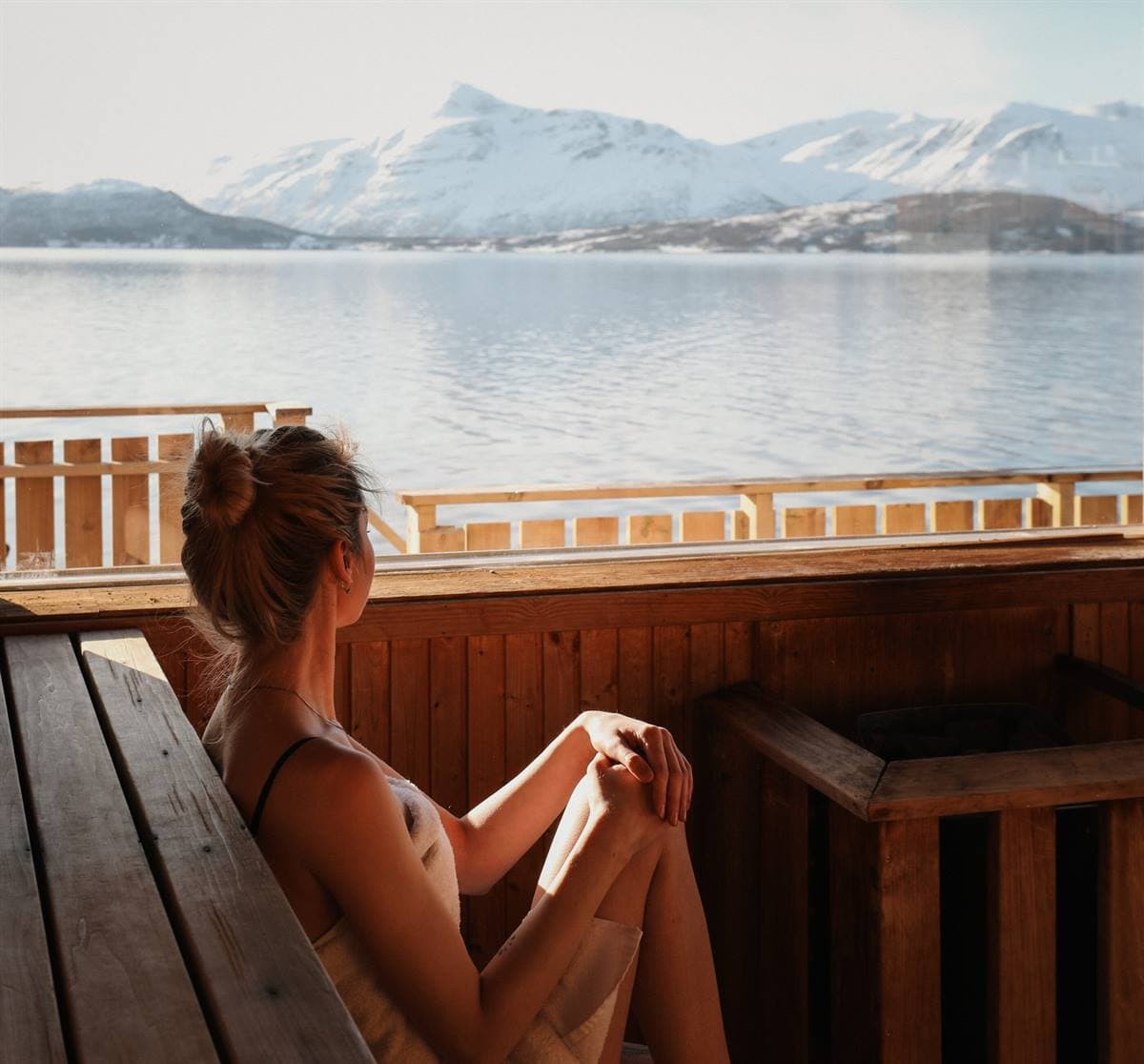 Guest in the sauna looking out over the fjord and snow-capped mountains