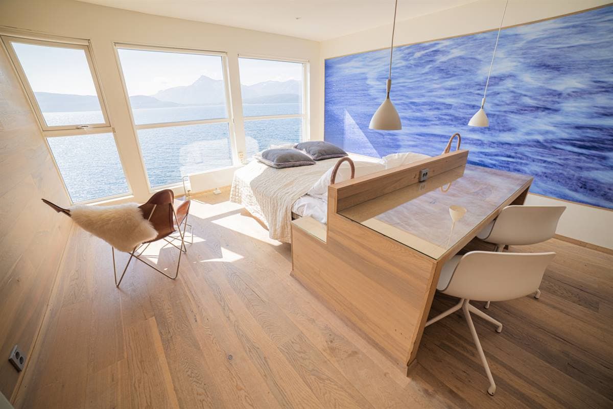 Desk and bed under a wave mural, with windows towards the fjord