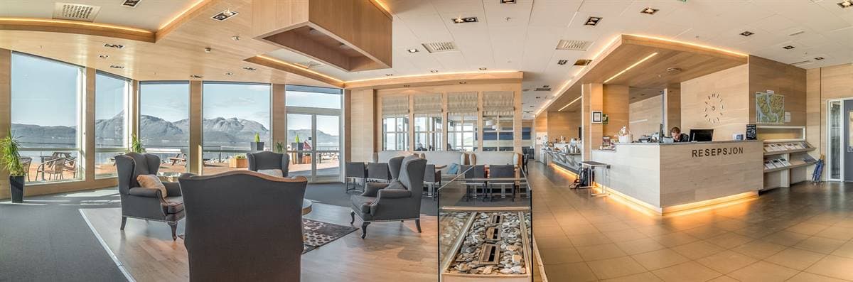 Lobby with reception, armchairs and tall windows facing the fjord and mountains