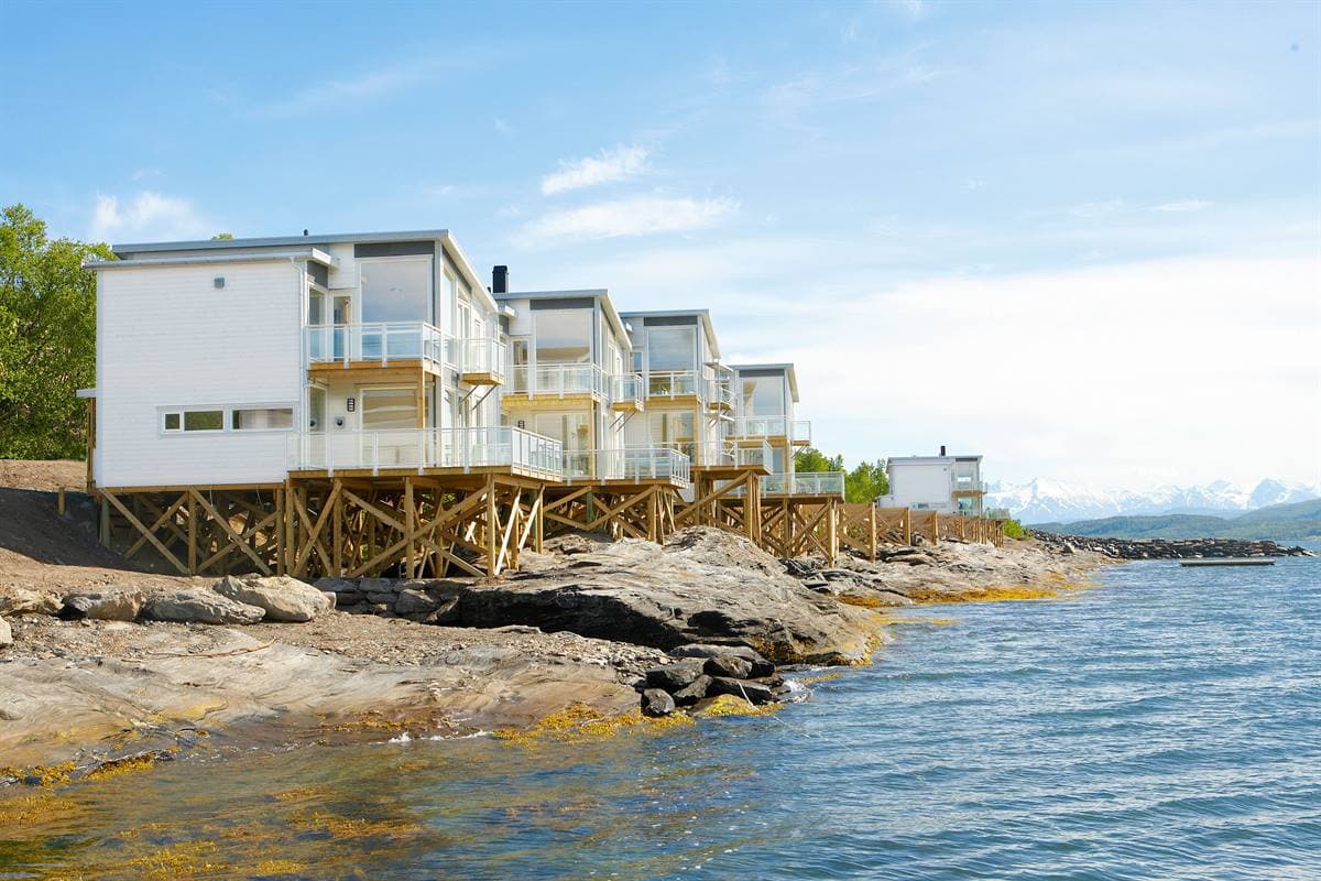 White two-storey Waterfront Premium Cabins on wooden stilts over the shoreline rocks in summer
