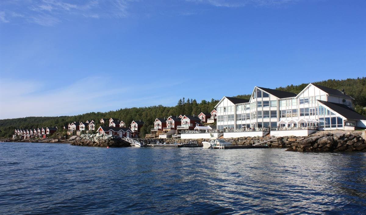 Malangen Resort seen from the fjord on a summer day, with the white main building and red cabins along the shore